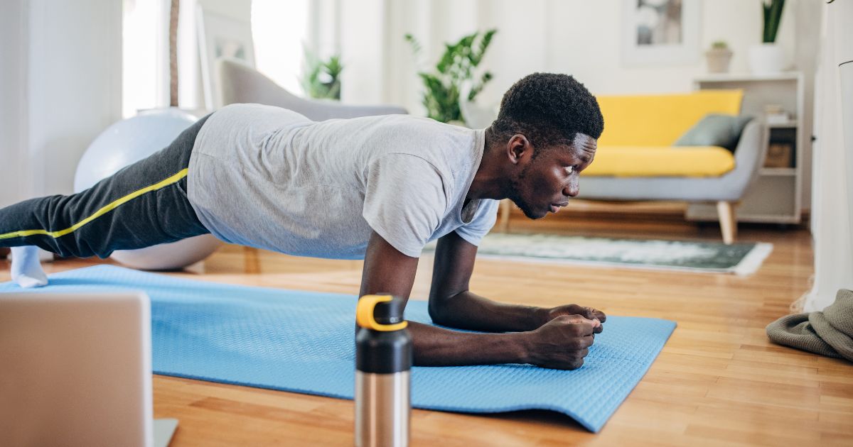 Man performing a plank exercise on a blue yoga mat in a bright, modern living room, emphasizing core strength and posture improvement.