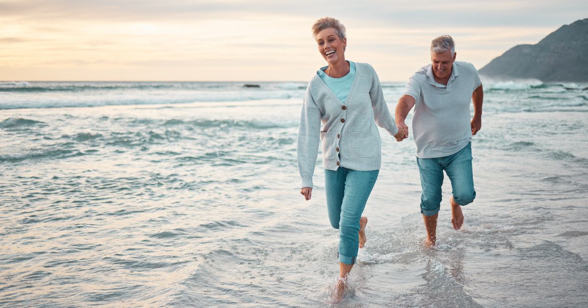 Couple joyfully walking hand in hand along the beach, splashing in the waves during sunset, symbolizing the benefits of spending time in nature for stress relief and overall well-being.