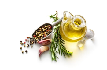 Olive oil, garlic, fresh rosemary, and mixed peppercorns arranged on a white background, highlighting key ingredients of the Mediterranean diet.