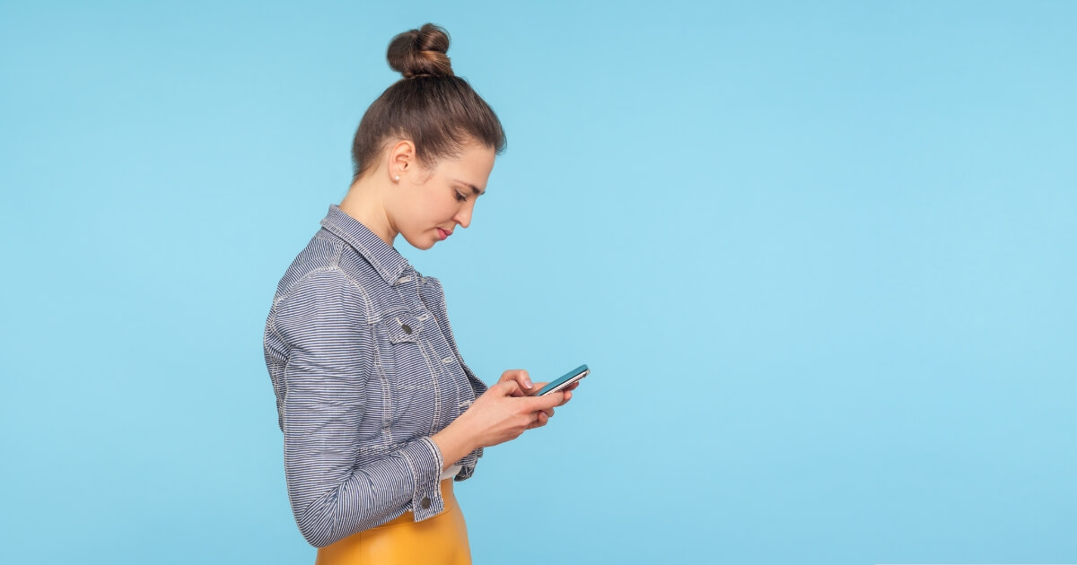Woman in a striped jacket looking down at smartphone against a light blue background, illustrating the impact of poor posture on daily activities.