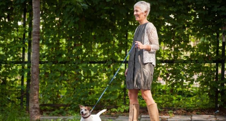 Woman walking a small dog in a park setting, surrounded by greenery, promoting outdoor activity and wellness.