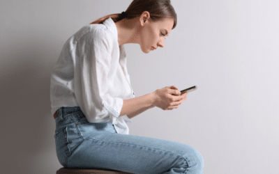 Woman sitting with poor posture while using a smartphone, illustrating the impact of smartphone use on spinal health and posture.